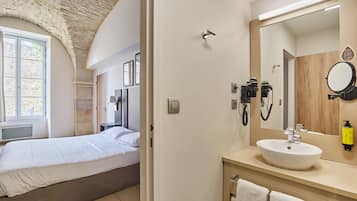 Une chambre avec un lit, une salle de bain avec un lavabo et un miroir, et un plafond en pierre.