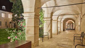 An indoor courtyard with stone arches, benches, and a grassy area with flowers. - Appart'hôtel Odalys City - Dijon Centre Les Cordeliers (Dijon)