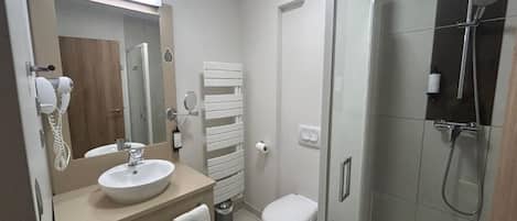 A modern bathroom with a sink, mirror, towel rack, toilet, and a glass-enclosed shower area.