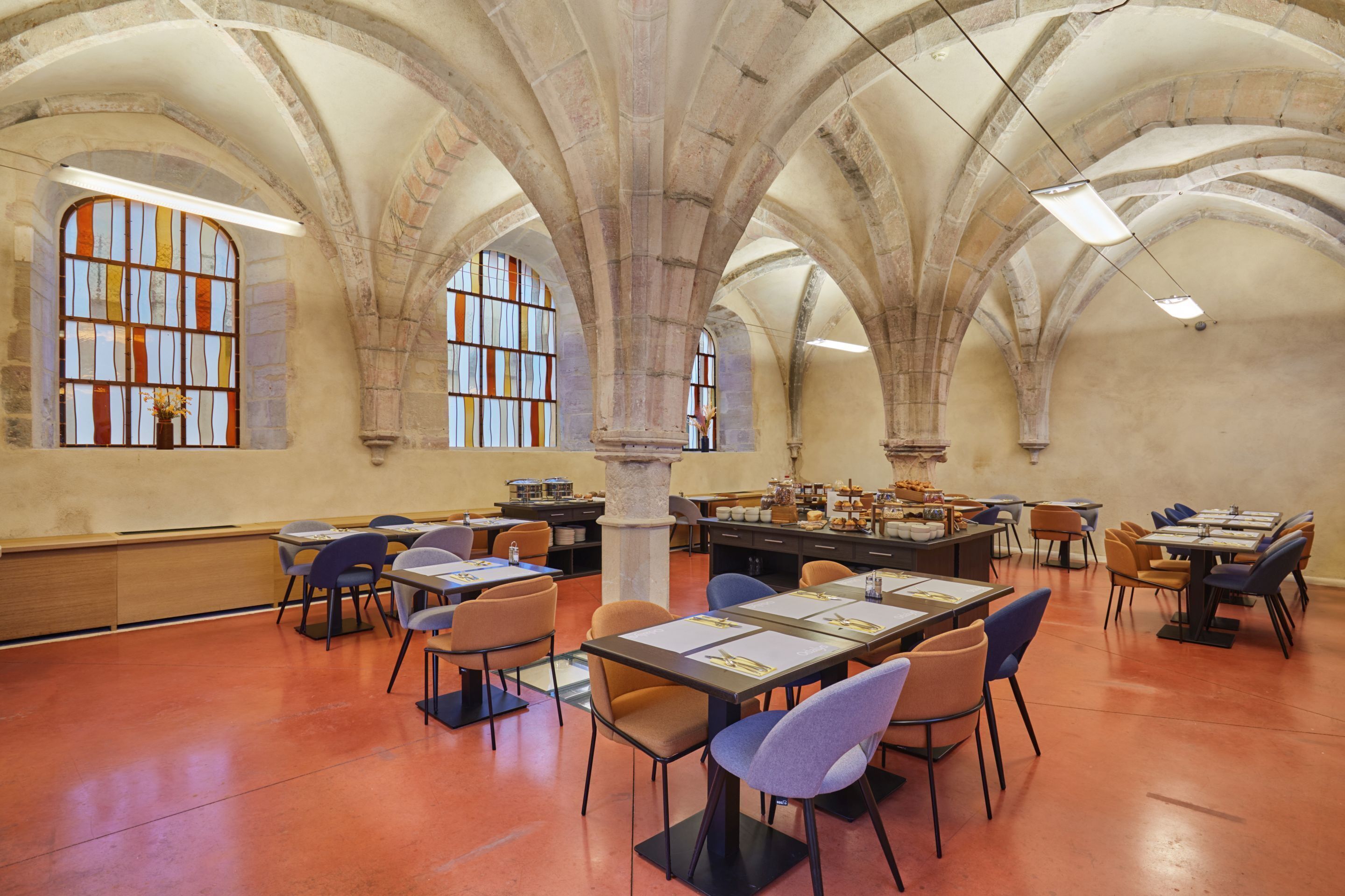 A spacious library with high arched ceilings, multiple tables and chairs, and large stained glass windows.