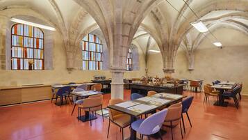 A spacious library with high arched ceilings, multiple tables and chairs, and large stained glass windows.