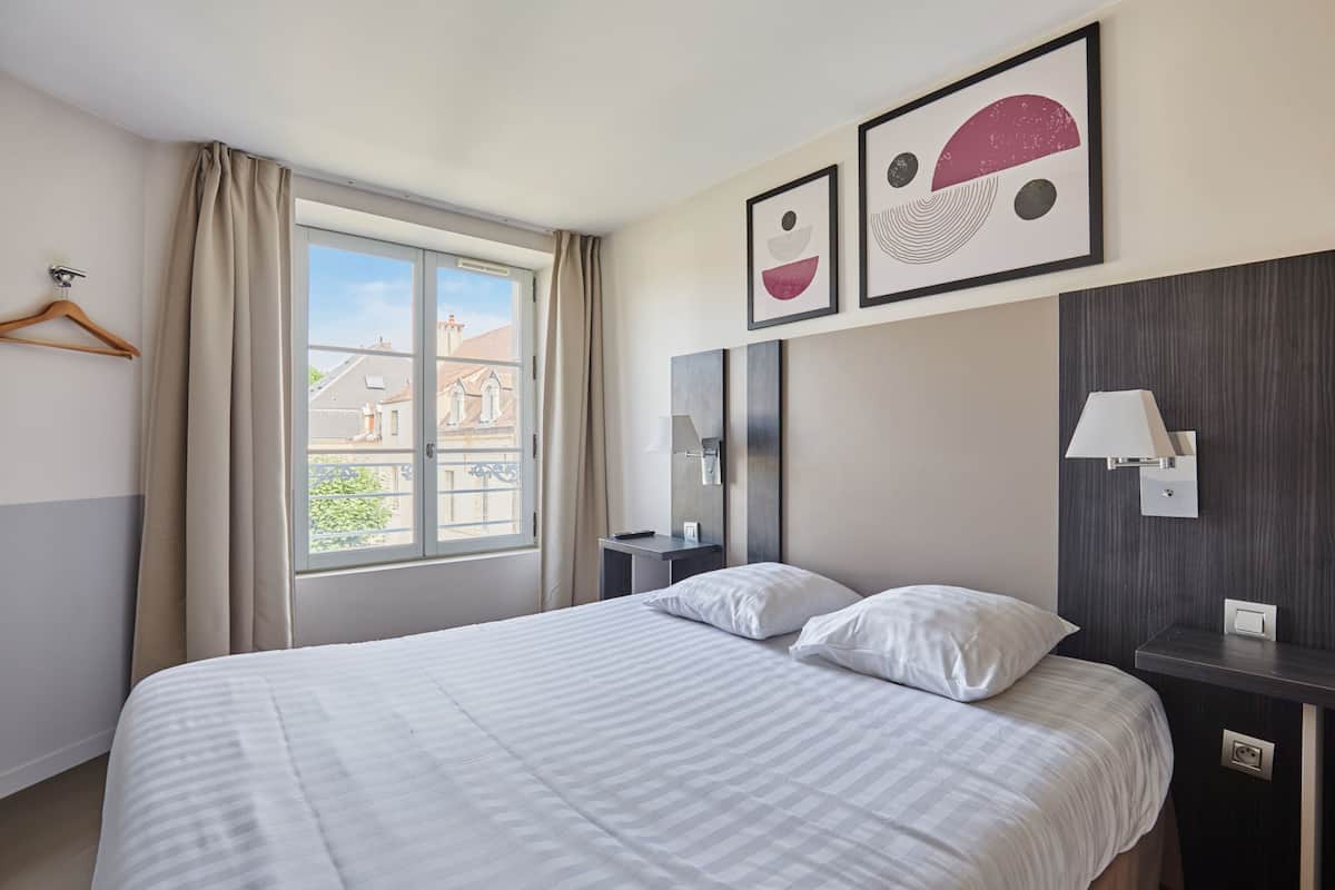 Quarto de hotel com uma cama grande, mesa de cabeceira, espelho e janela com cortinas.