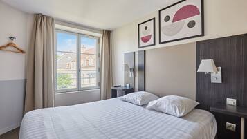 A hotel room with a large bed, a bedside table, a mirror, and a window with curtains.