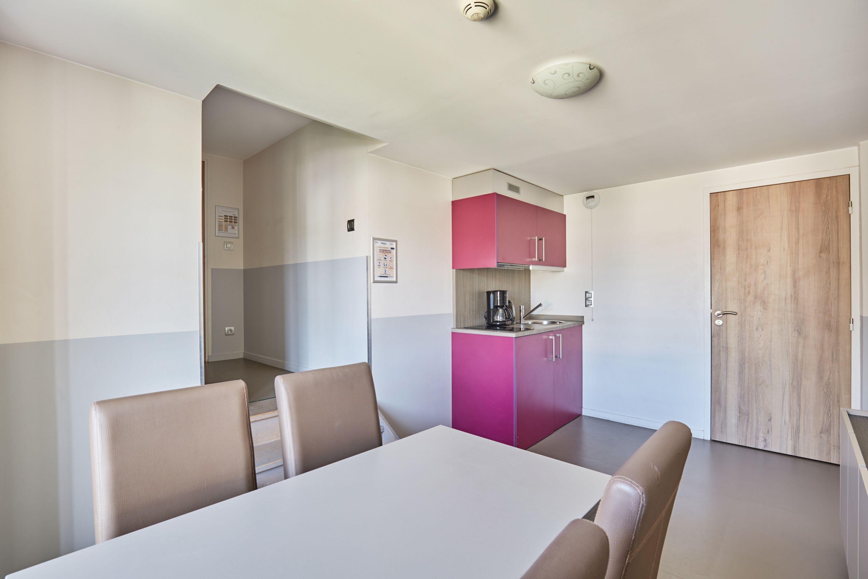 Quarto moderno com uma mesa de jantar e cadeiras, uma kitchenette com armários cor-de-rosa e uma porta de madeira.