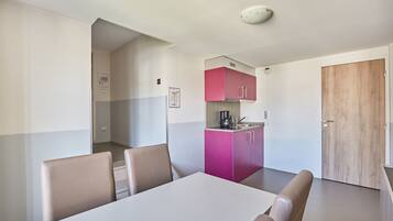 Quarto moderno com uma mesa de jantar e cadeiras, uma kitchenette com armários cor-de-rosa e uma porta de madeira.