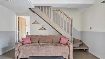 A modern living room with a beige sofa, a wooden staircase, and a door leading to another room.