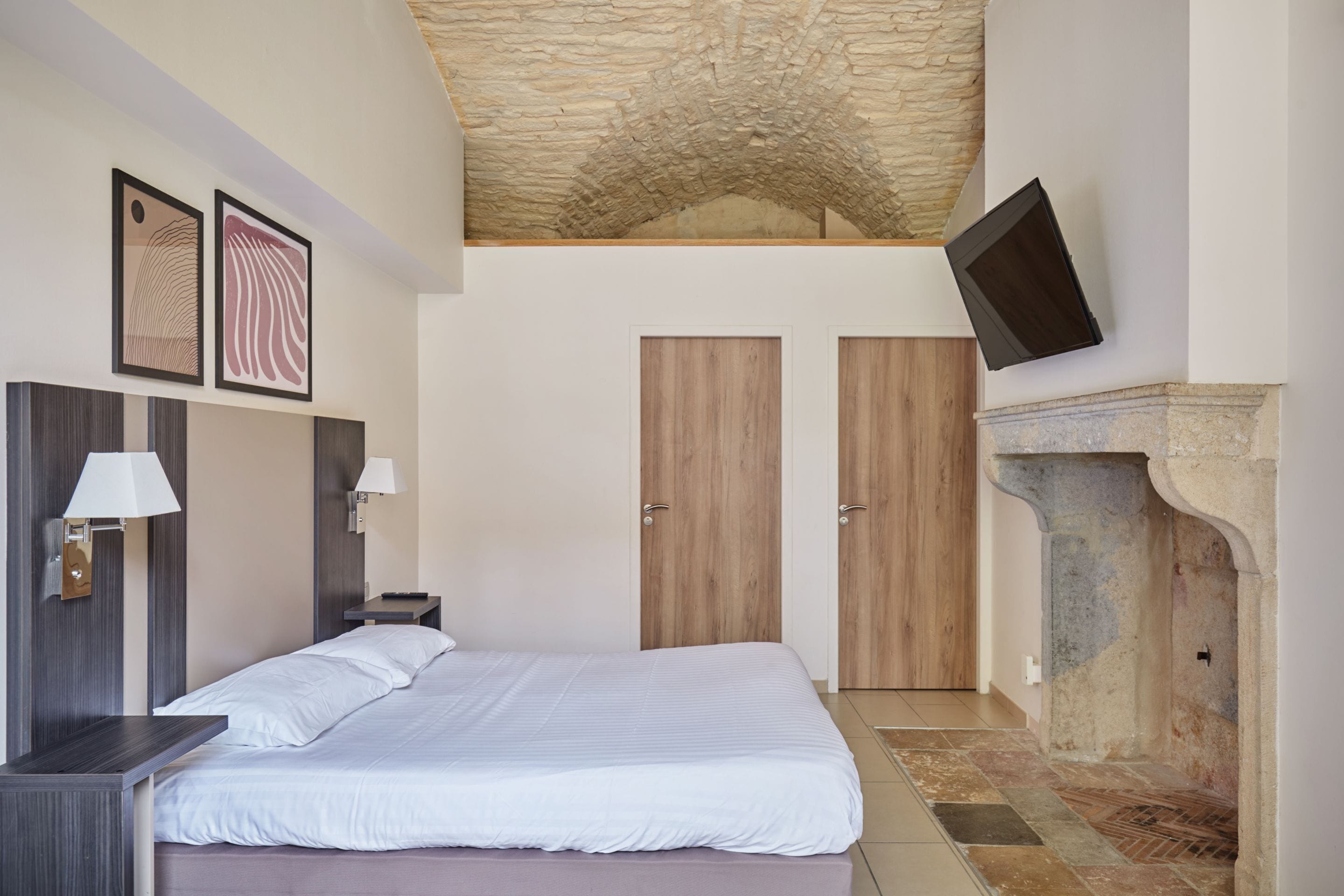 Une chambre à coucher avec un lit, des tables de chevet, un téléviseur fixé au mur et une cheminée en pierre.
