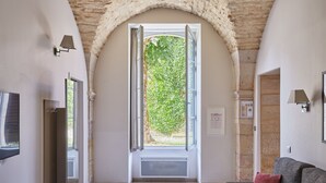A room with a stone archway leading to a balcony, a grey sofa with a red pillow, and a flat-screen TV on the left. - Appart'hôtel Odalys City - Dijon Centre Les Cordeliers (Dijon)