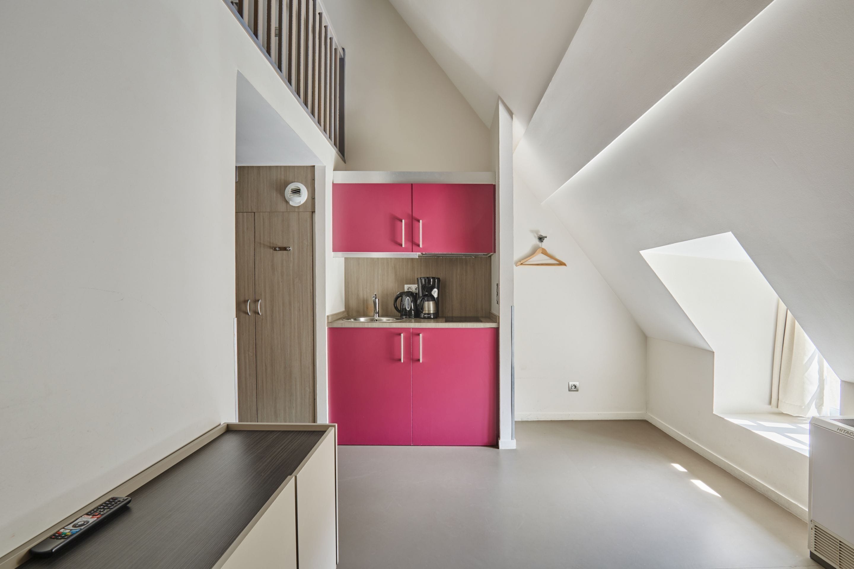 Une cuisine moderne avec des armoires roses, une porte en bois et un porte-manteau suspendu.