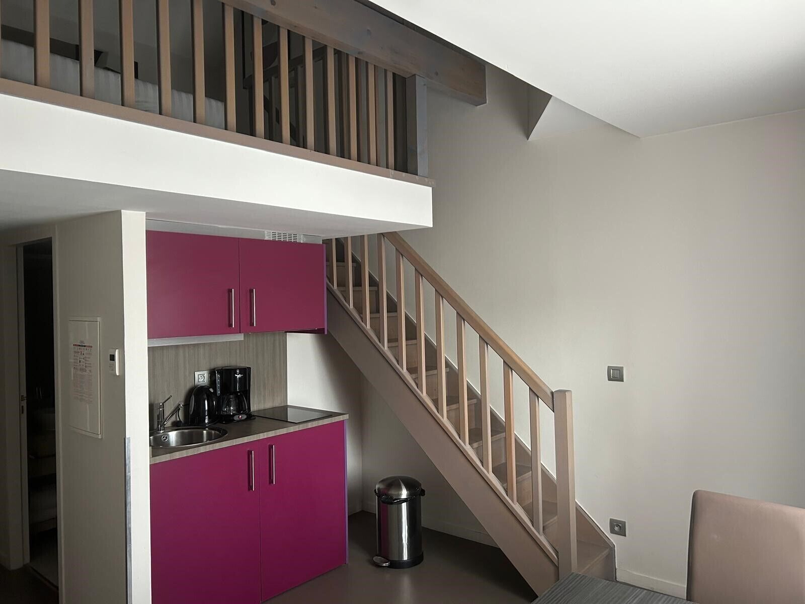 A compact kitchen with pink cabinets, a coffee maker, and a trash can.