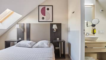 A modern hotel room with a skylight, a bed with white bedding, two bedside tables with lamps, a framed artwork on the wall, and a bathroom with a sink and mirror.
