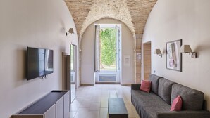A modern living room with a stone ceiling, a flat-screen TV, a sofa with cushions, and a small table. - Appart'hôtel Odalys City - Dijon Centre Les Cordeliers (Dijon)