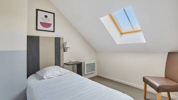 Ein Schlafzimmer mit Bett, Sessel, Nachttisch, Lampe, Fernseher und Dachfenster.