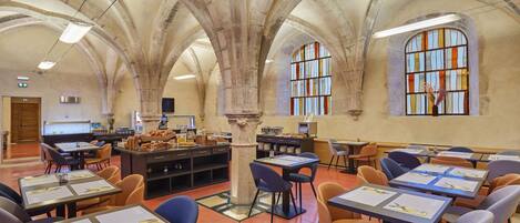 A spacious dining area with high arched ceilings and large windows, featuring tables set with menus and cutlery.