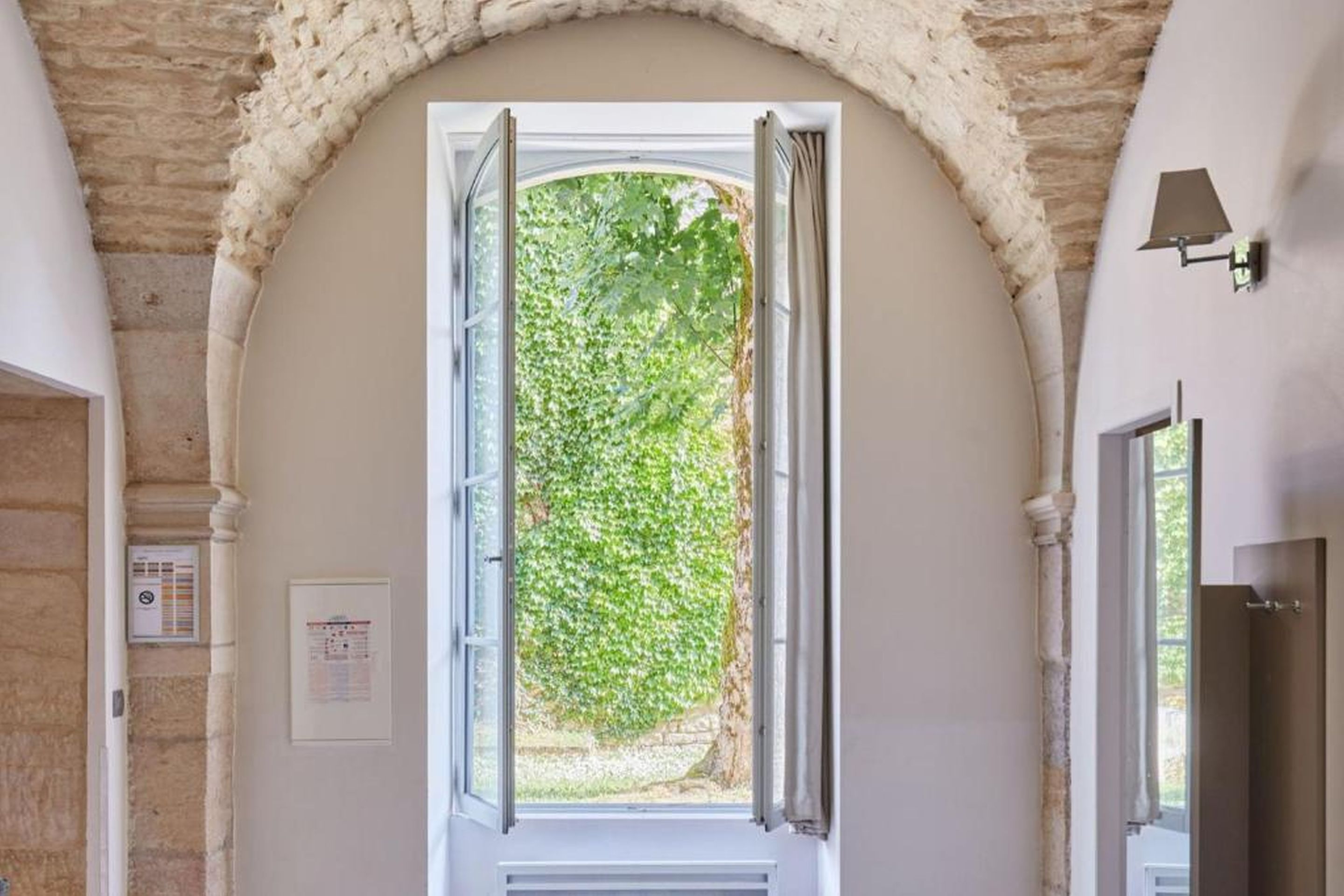 Une porte en arc surmontée d’une fenêtre ouverte donnant sur un jardin.