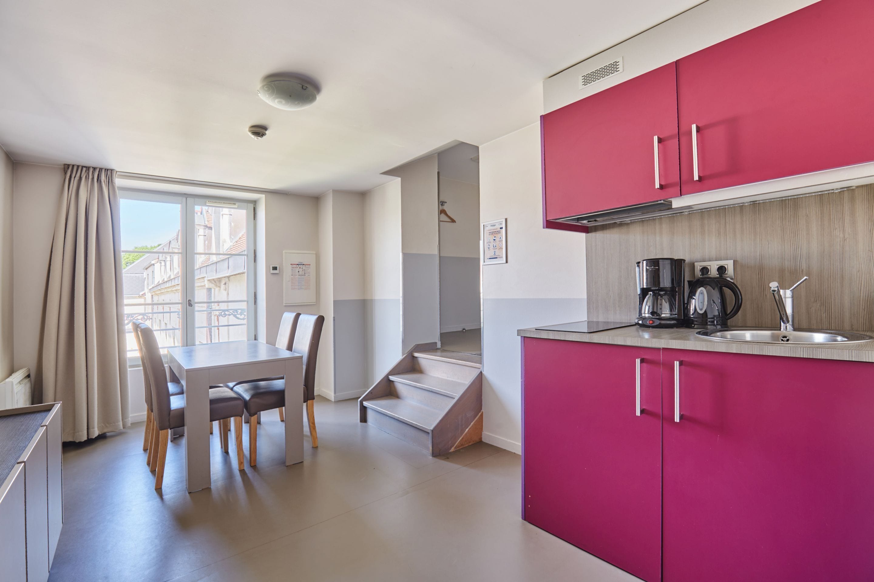 A modern kitchen with pink cabinets, a dining area with a table and chairs, and a staircase leading to another level.