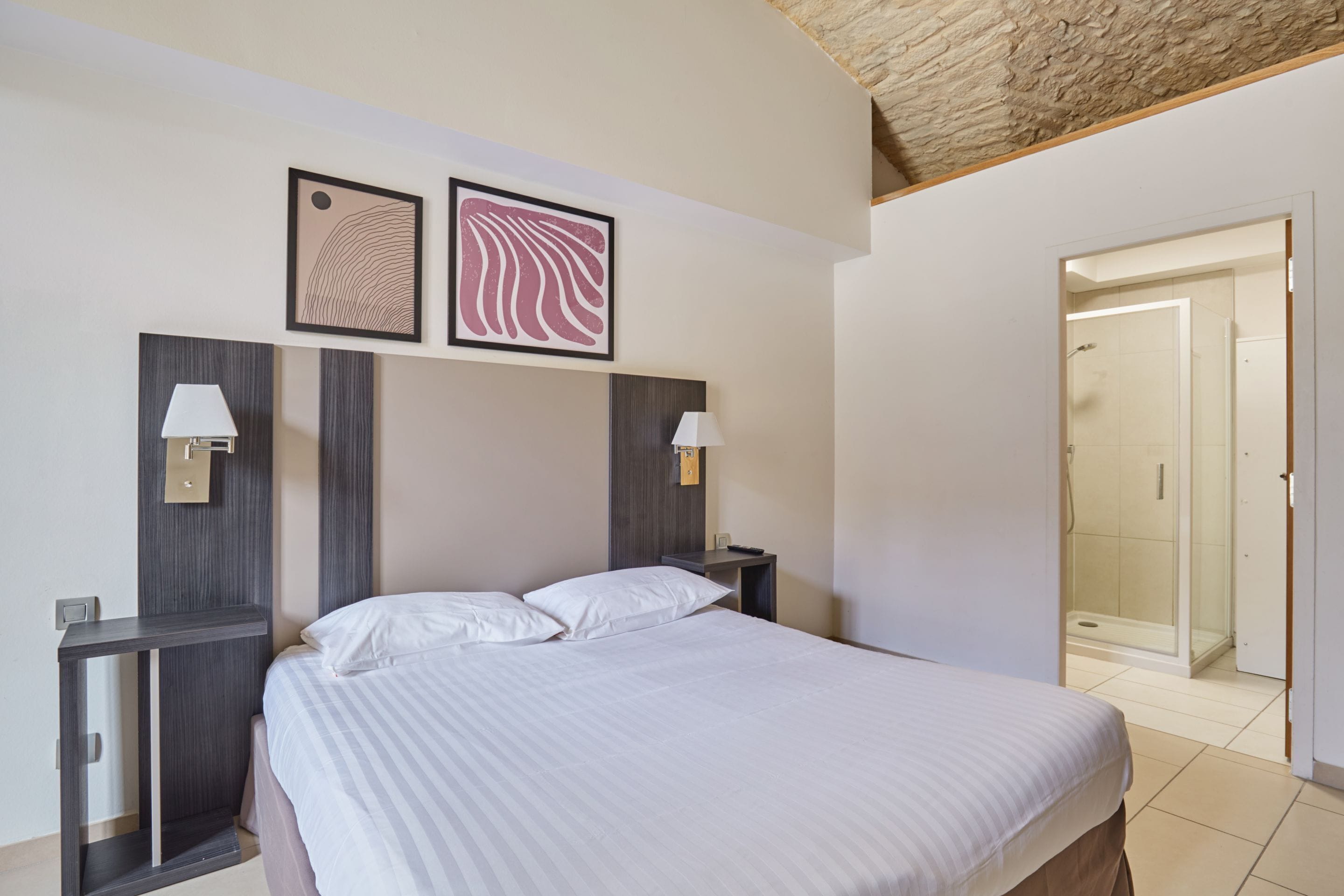 A hotel room with a large bed, two bedside tables with lamps, a wooden headboard, and two framed pictures on the wall.