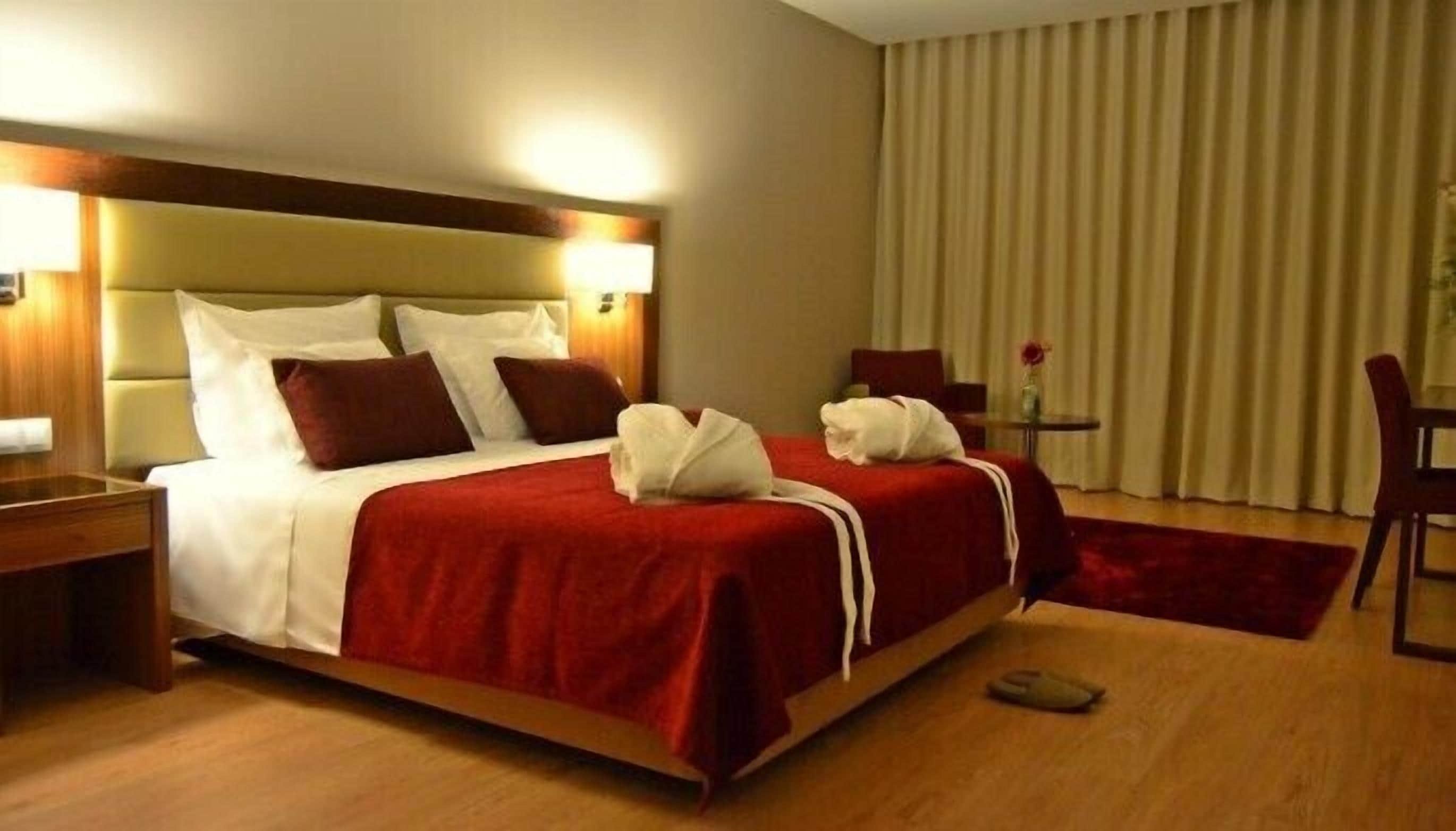 Habitación de hotel con una cama grande, una mesita de noche, una silla y una pequeña mesa con un florero.
