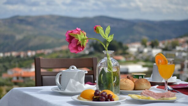 Una mesa dispuesta para el desayuno, con pan, huevos, jamón y fruta, un florero y un vaso de zumo de naranja.