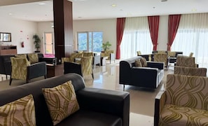 A hotel lobby with a reception desk, seating area with sofas and chairs, large windows with curtains, and a plant. - Plácido Hotel Douro - Tabuaço (Tabuaço)