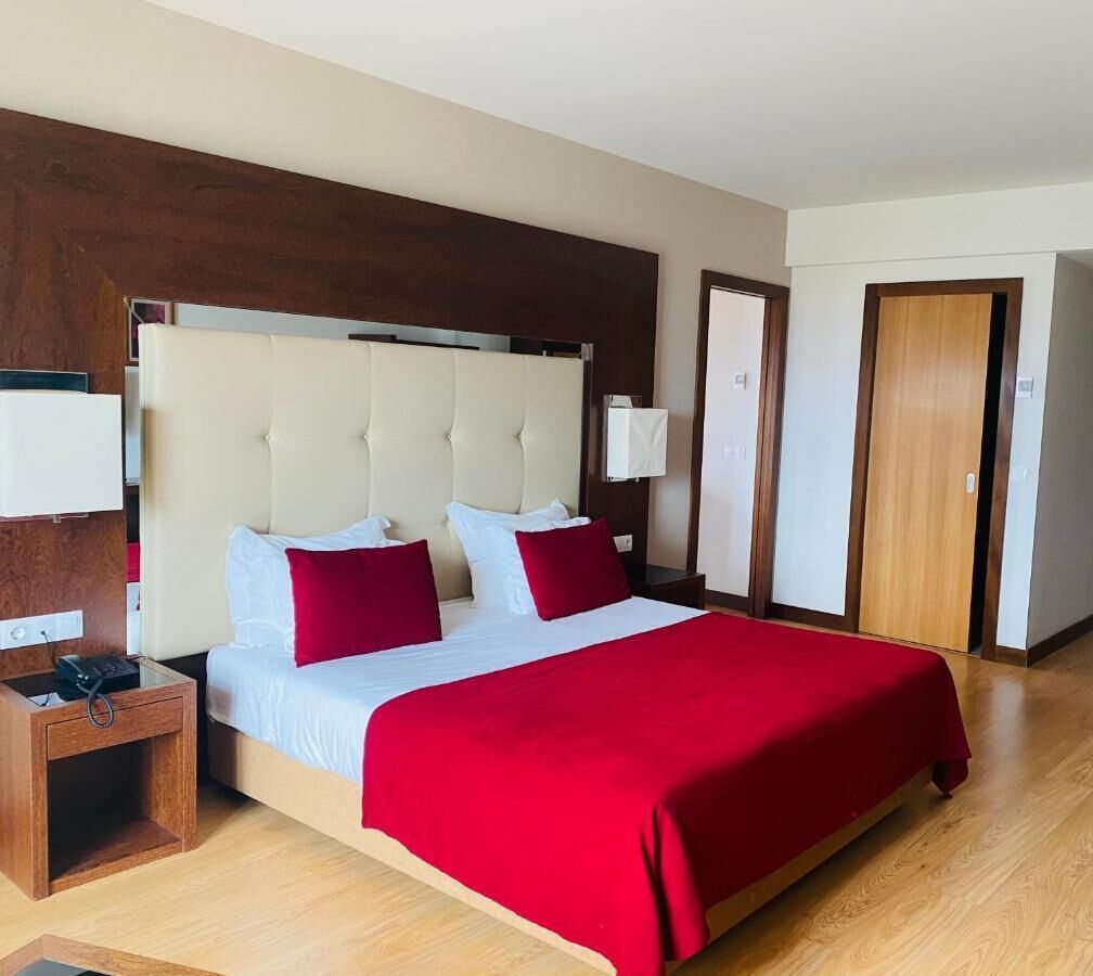 A hotel room with a large bed, a bedside table with a phone, a wooden nightstand, and a wardrobe.