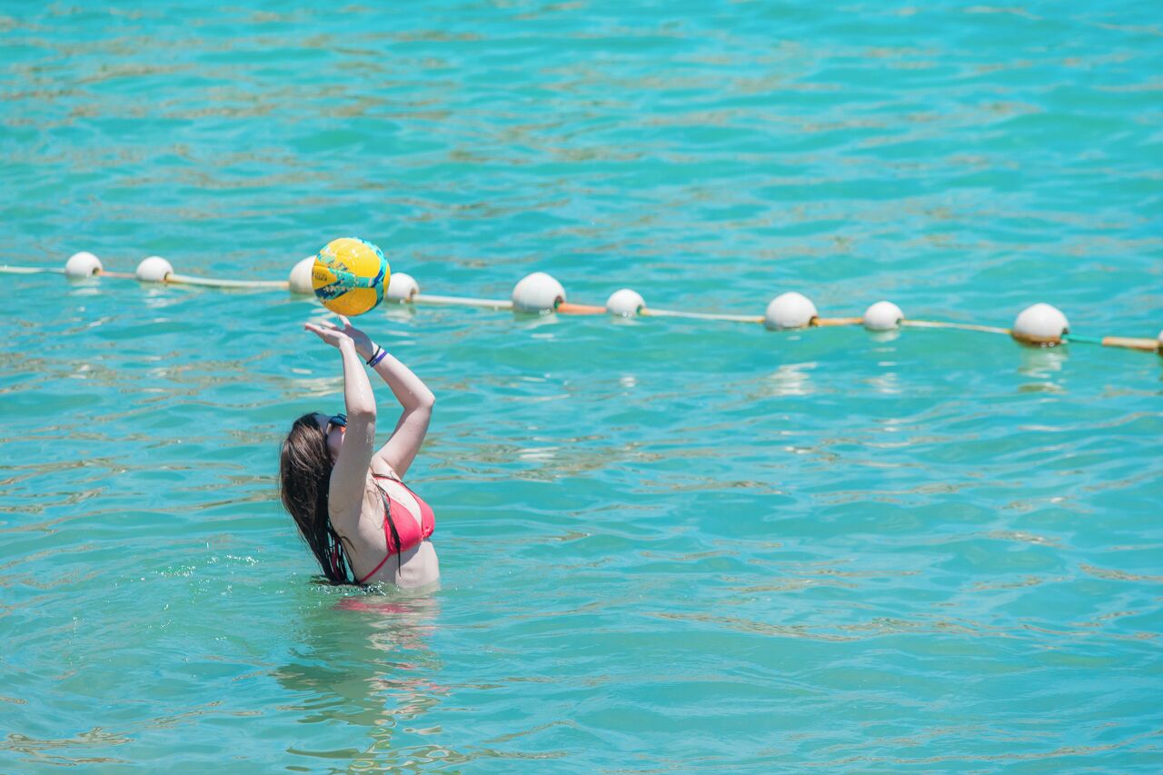 A person in a pool with a yellow ball, water, and lane markers.