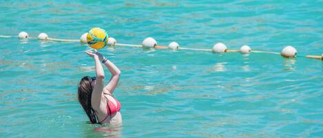A person in a pool with a yellow ball, water, and lane markers.