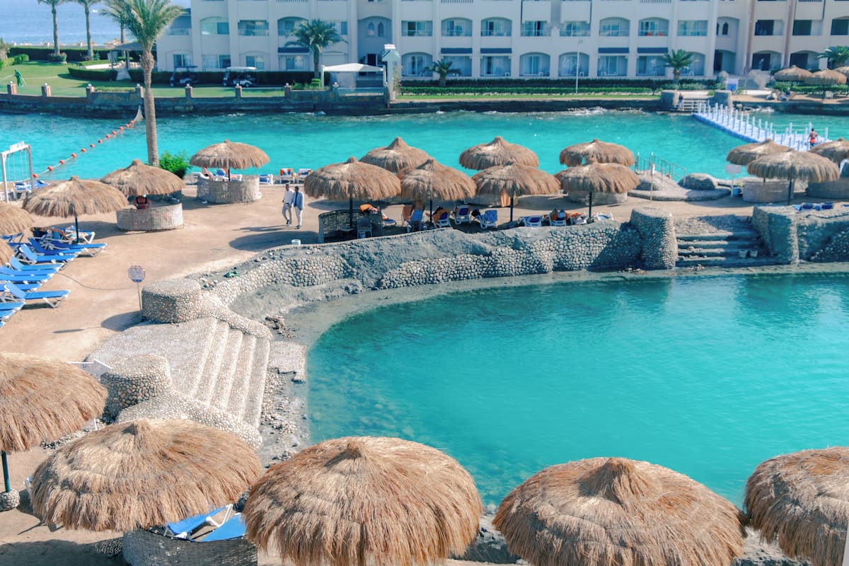 Un complexe hôtelier doté d’une piscine, de chaises de plage et de parasols en chaume.
