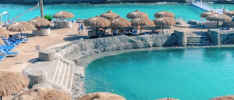 A resort with a pool, beach chairs, and thatched umbrellas.