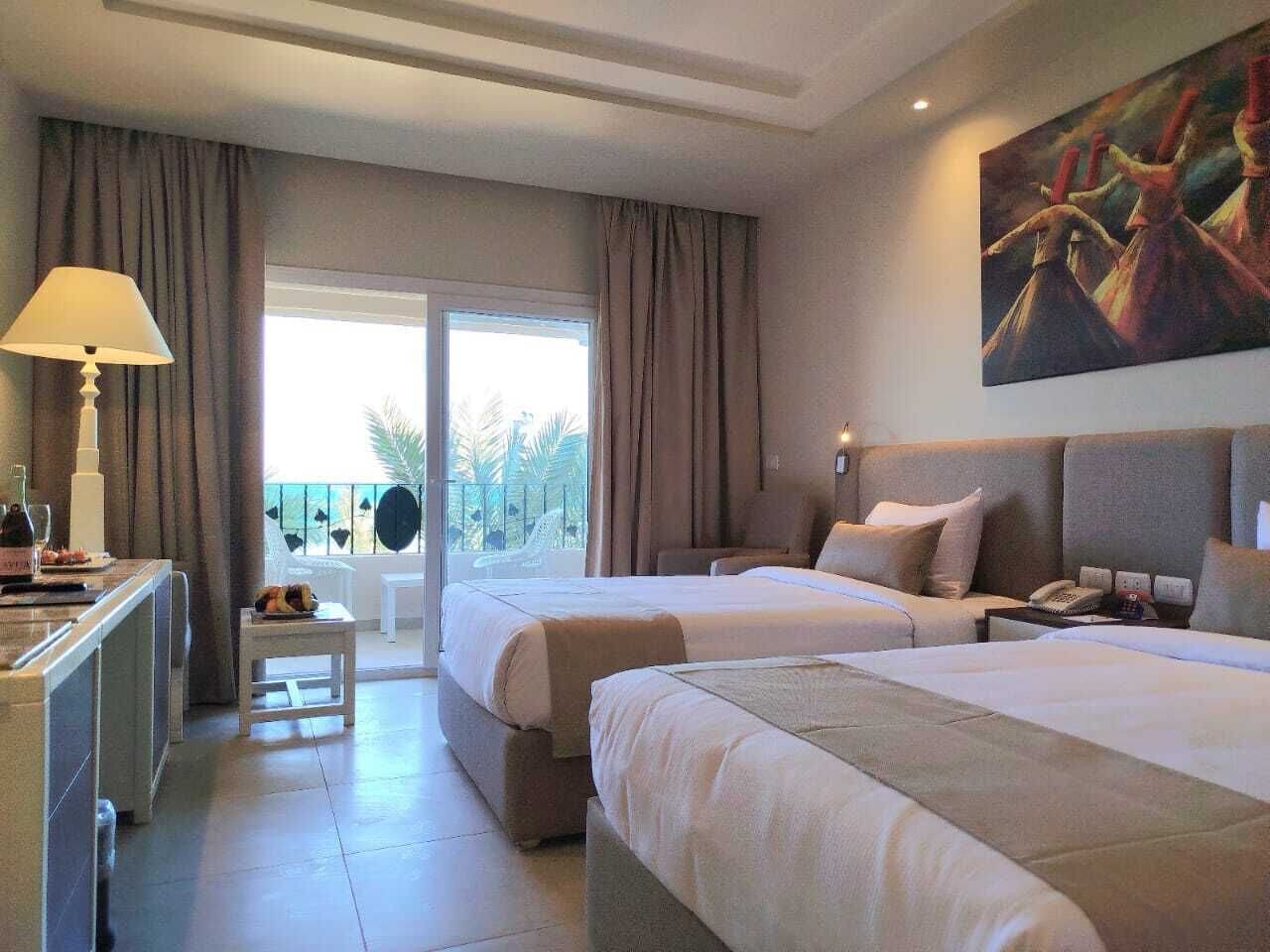 Habitación de hotel con dos camas, un escritorio, una silla y un balcón con vistas.