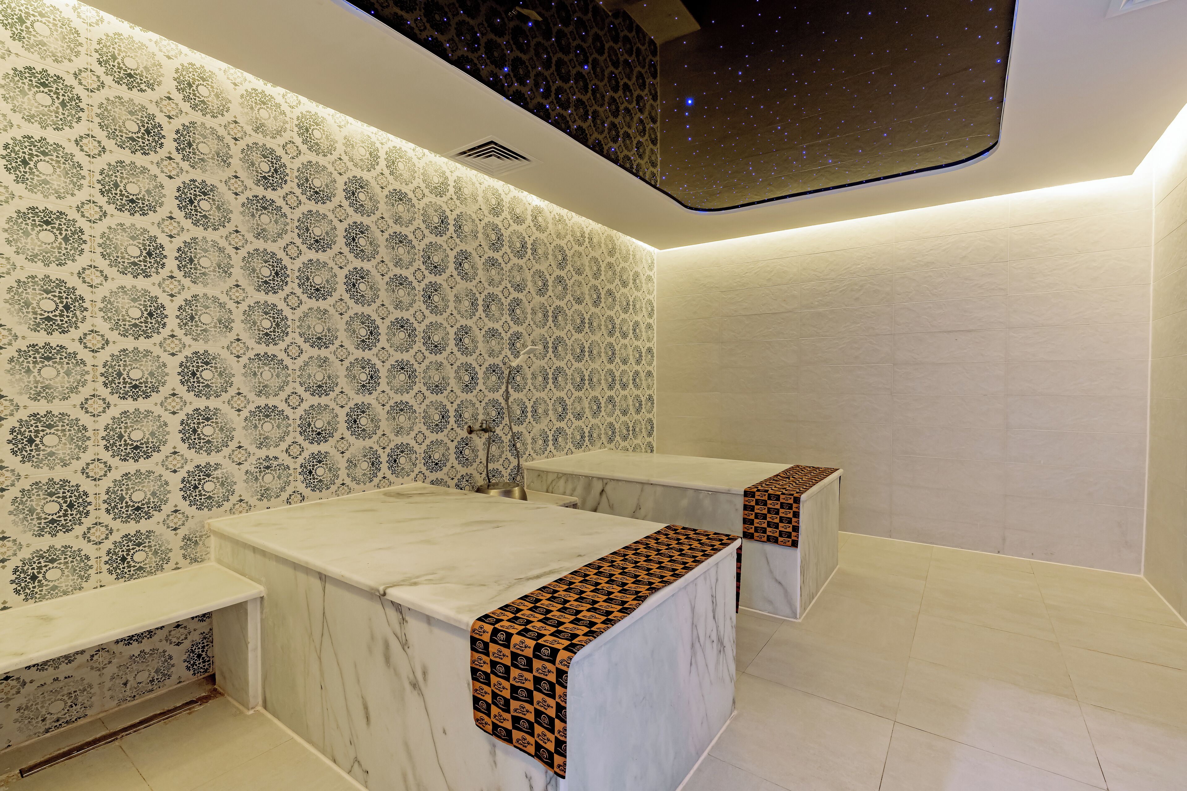 Un baño con papel tapiz estampado, encimeras de mármol y un diseño de techo que simula un cielo estrellado.