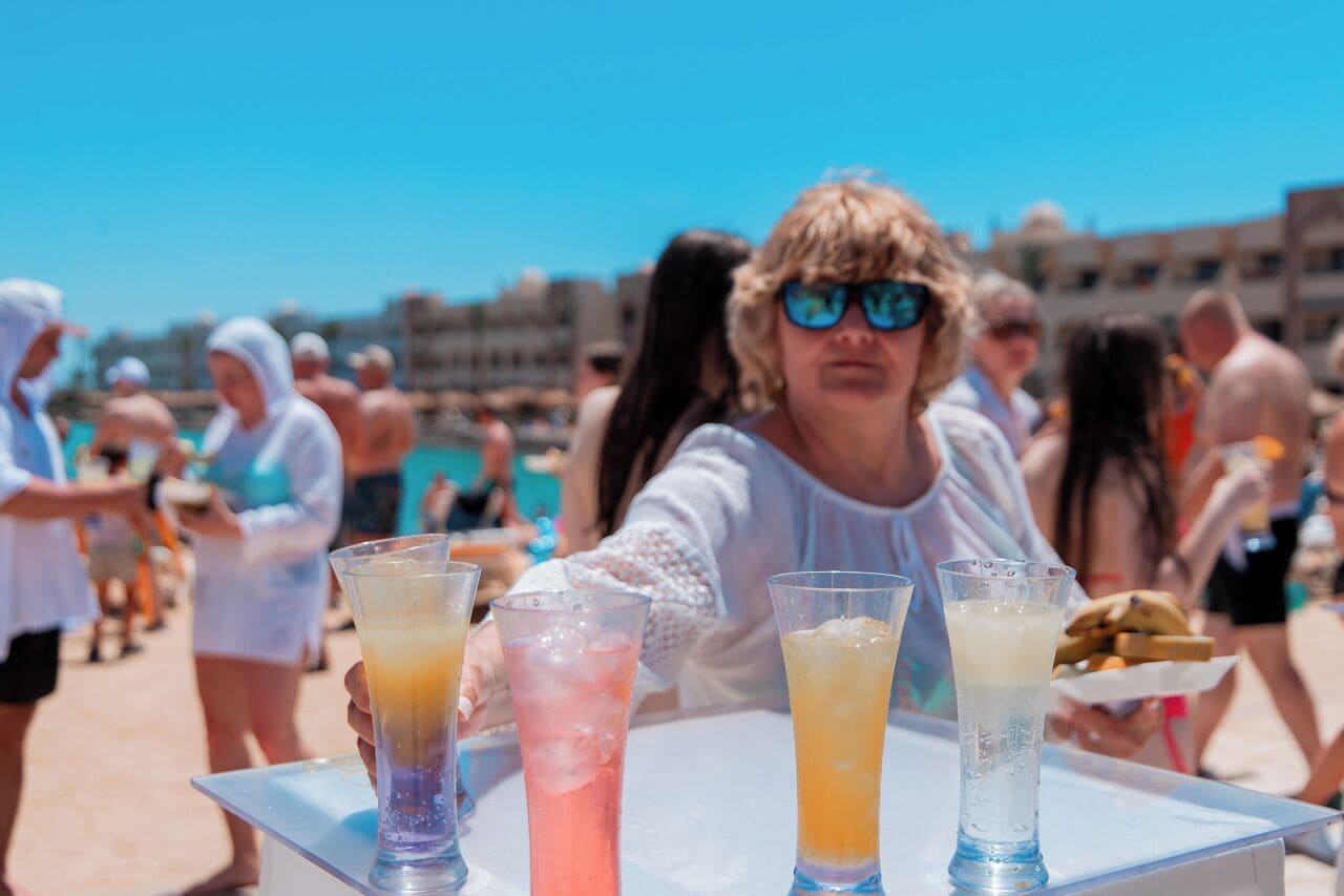 A beach scene with people, a table with drinks, and a clear blue sky.