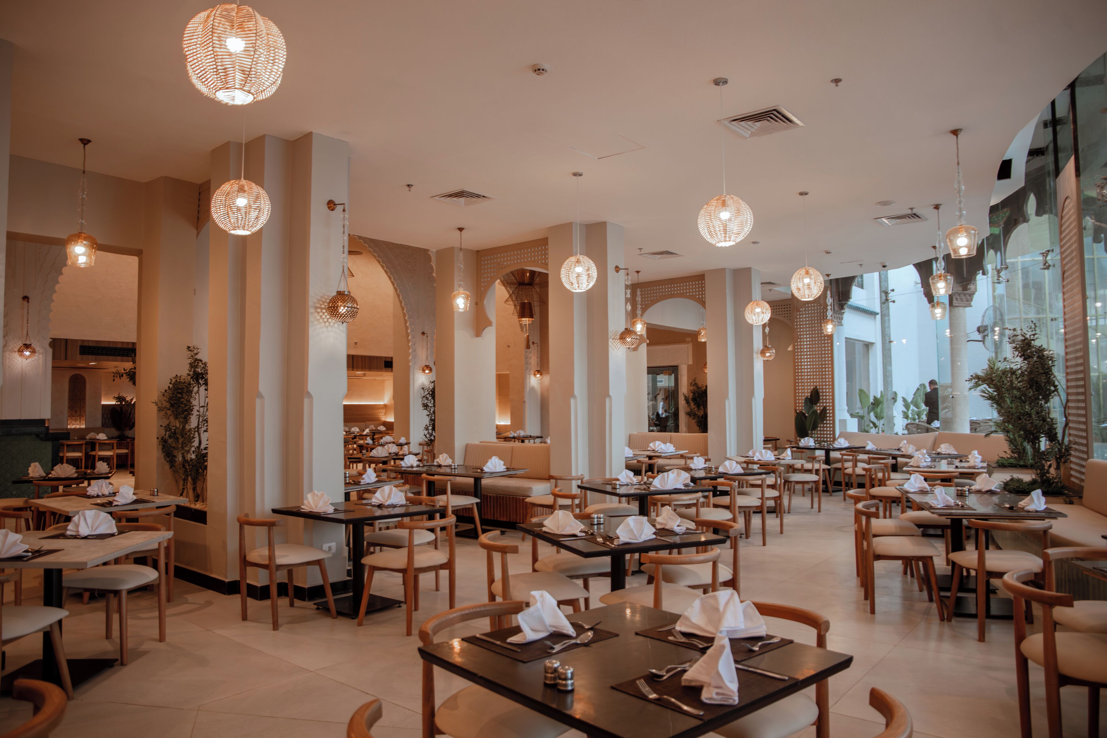 A spacious restaurant with multiple dining tables and chairs, high ceilings, and hanging spherical light fixtures.