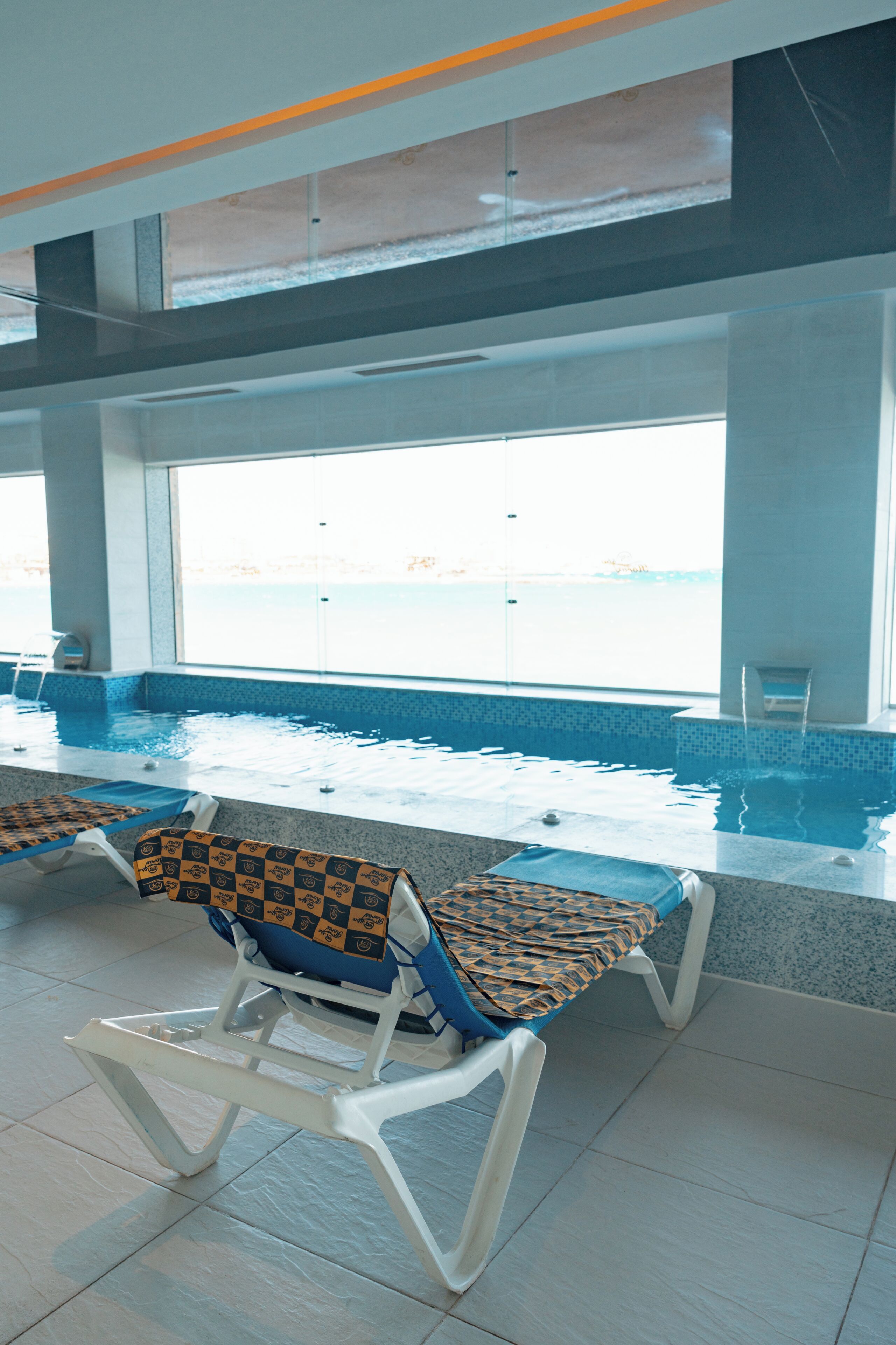 Un espace piscine avec des chaises longues et une vue sur la mer grâce à de grandes fenêtres.