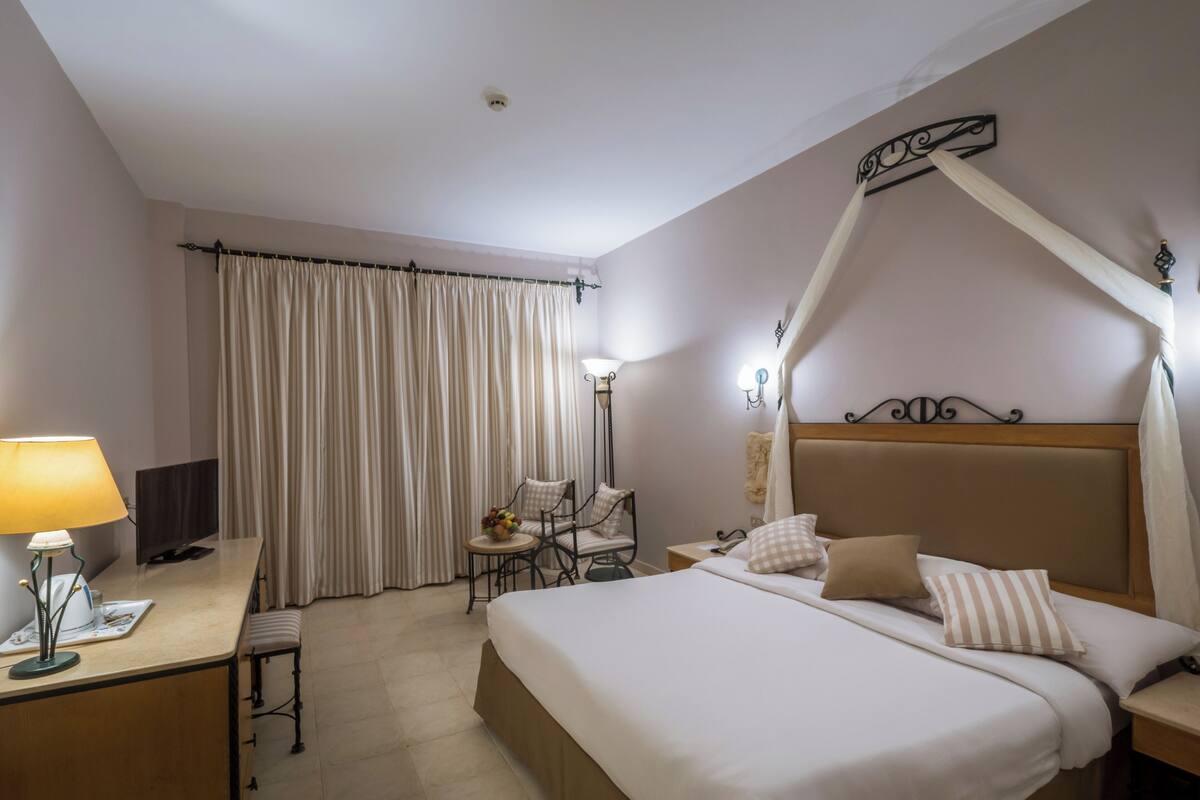 Une chambre d’hôtel avec un lit, une table de chevet, une lampe, une chaise et des rideaux.