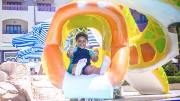 Un niño o niña se desliza por un tobogán acuático colorido con una piscina al final.