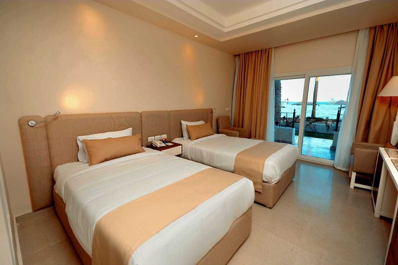 A hotel room with two beds, a desk, and a view of the sea.