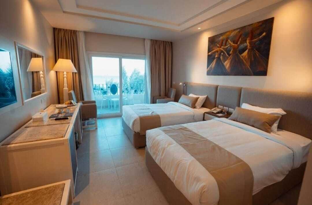 Habitación de hotel con dos camas, un escritorio, una silla, una lámpara y un cuadro en la pared.