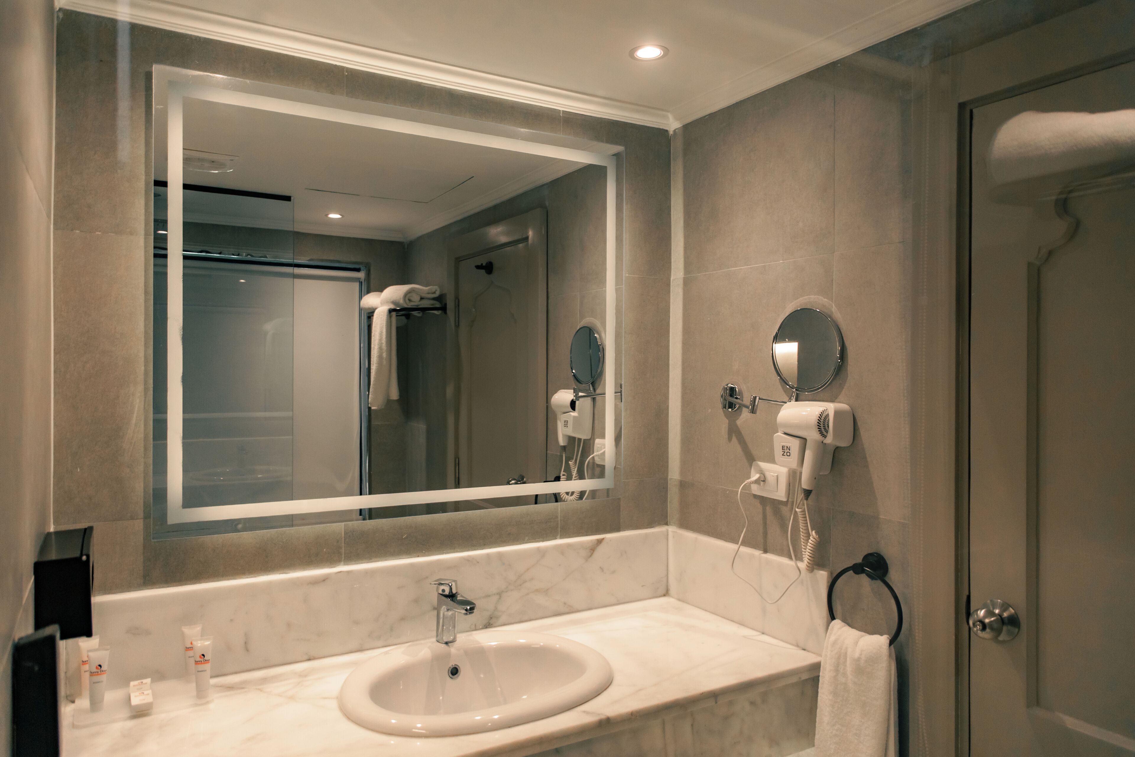 Un baño con un espejo grande, un lavabo, un perchero para toallas y un secador de pelo.