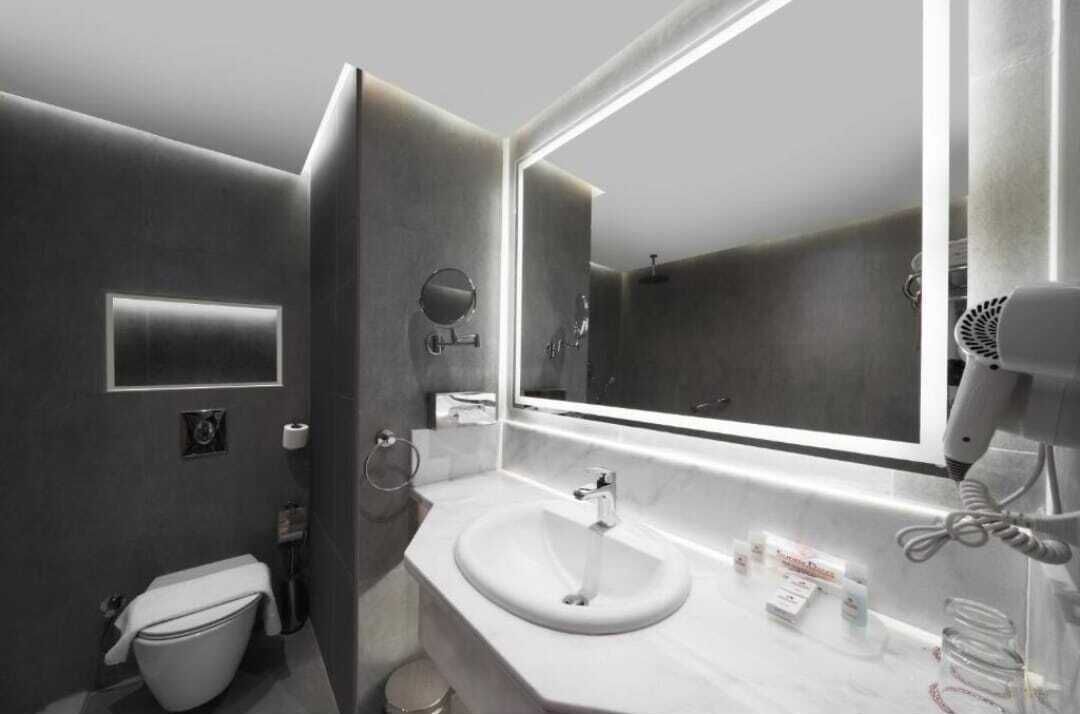 A modern bathroom with a large mirror, a sink, a toilet, and a hairdryer.