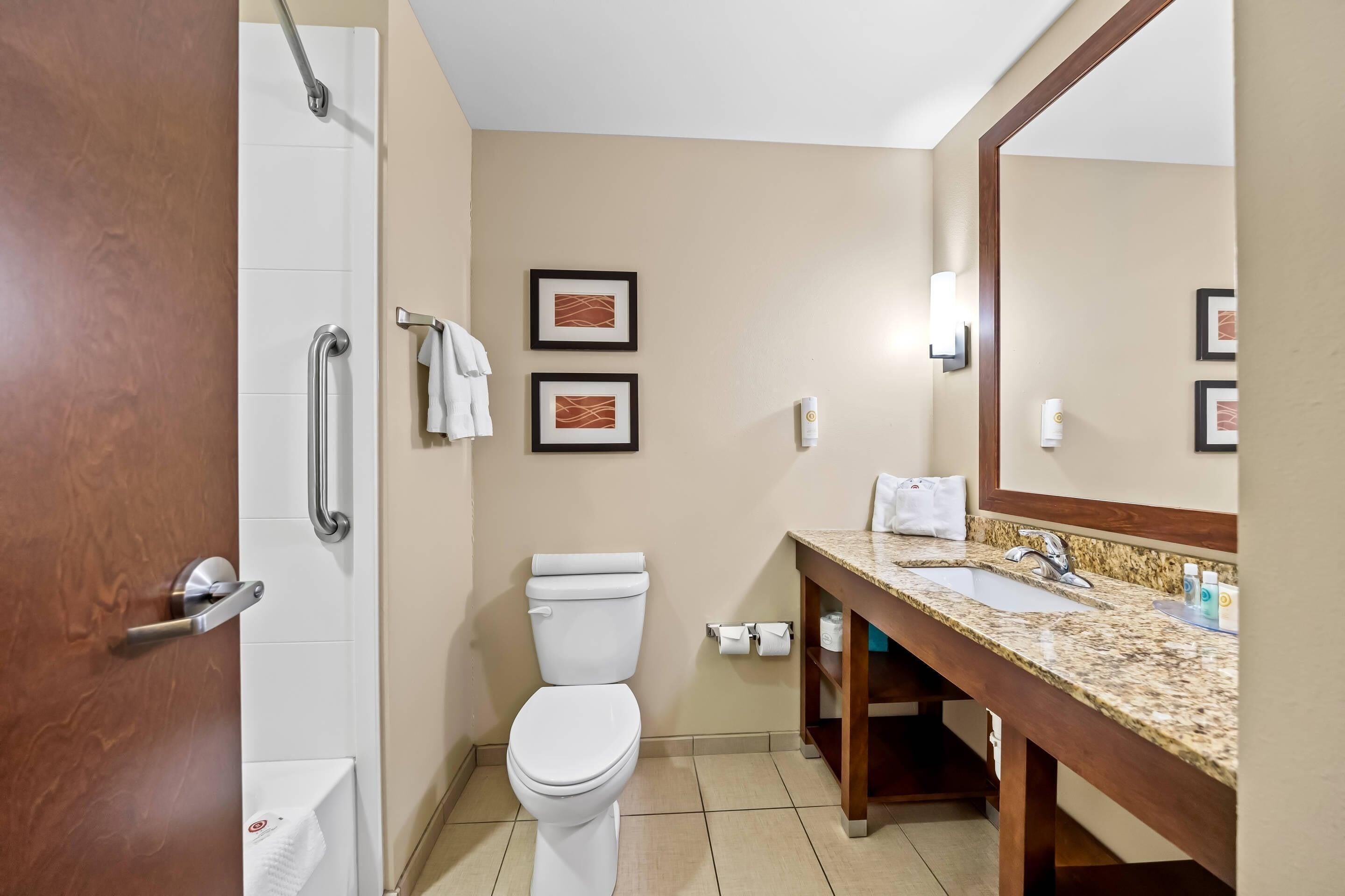 Une salle de bain avec des toilettes, un lavabo et une douche. On y trouve des serviettes et des tableaux encadrés accrochés au mur.