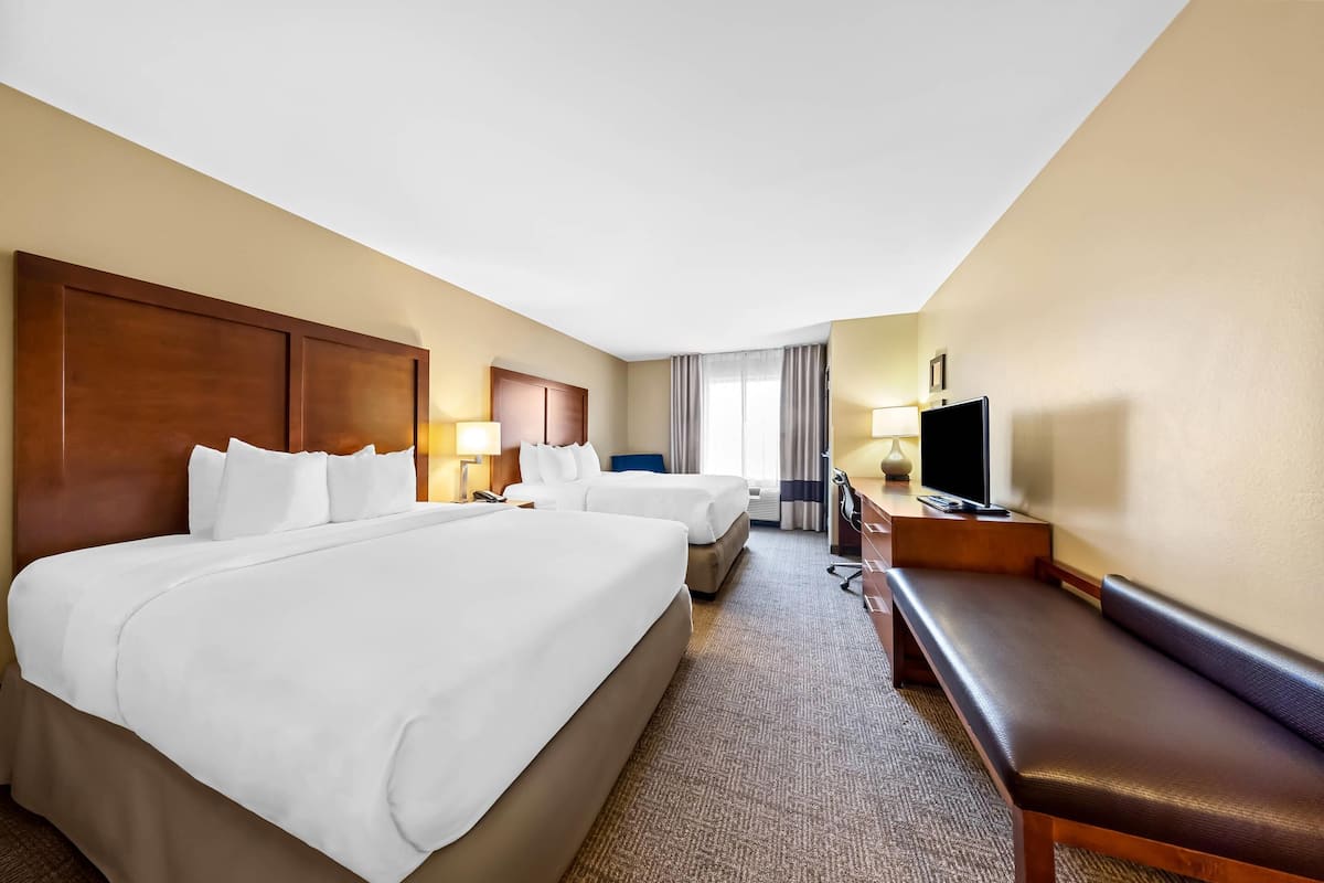 A hotel room with two beds, a desk, a TV, and a window with curtains.