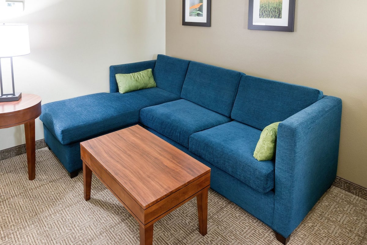 A blue sectional sofa with a wooden coffee table, a small round table, and two framed pictures on the wall.