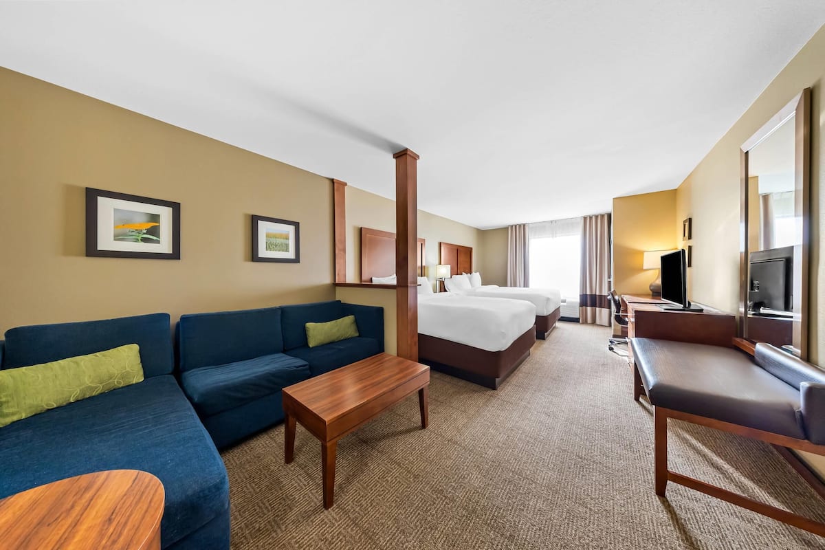A hotel room with a blue sofa, a wooden coffee table, a bed with white linens, a TV, and a large mirror.