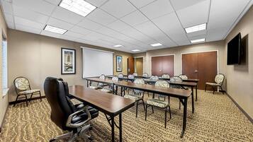 A conference room with a long table, chairs, a projector screen, and a television on the wall.