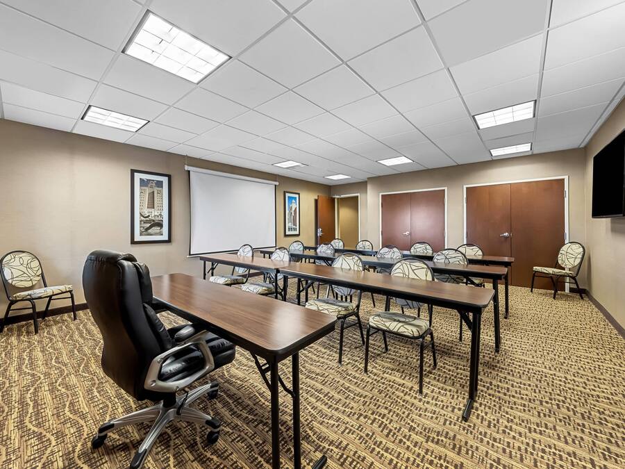 A conference room with a long table, chairs, a projector screen, and a television on the wall.