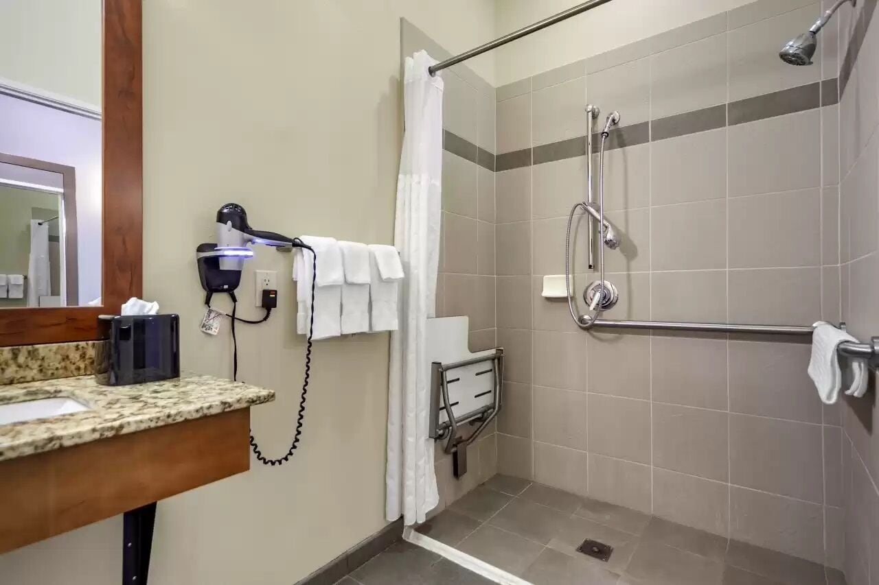 A bathroom with a shower, grab bars, a towel rack, and a hairdryer.