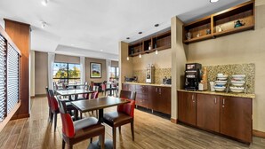 A modern dining area with wooden tables and chairs, a kitchen with granite countertops, and a view of the outdoors through large windows. - Comfort Inn & Suites West - Medical Center (Rochester)