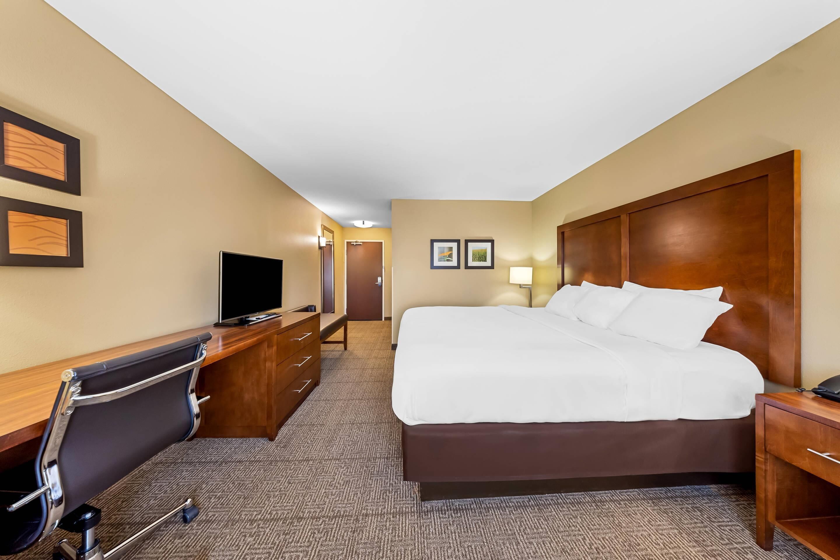 A hotel room with a large bed, a desk with a chair, a television, and a wooden headboard.
