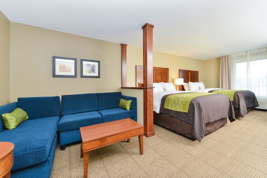 Habitación de hotel con un sofá azul, un banco de madera, una cama con dos almohadas y un pilar de madera grande.